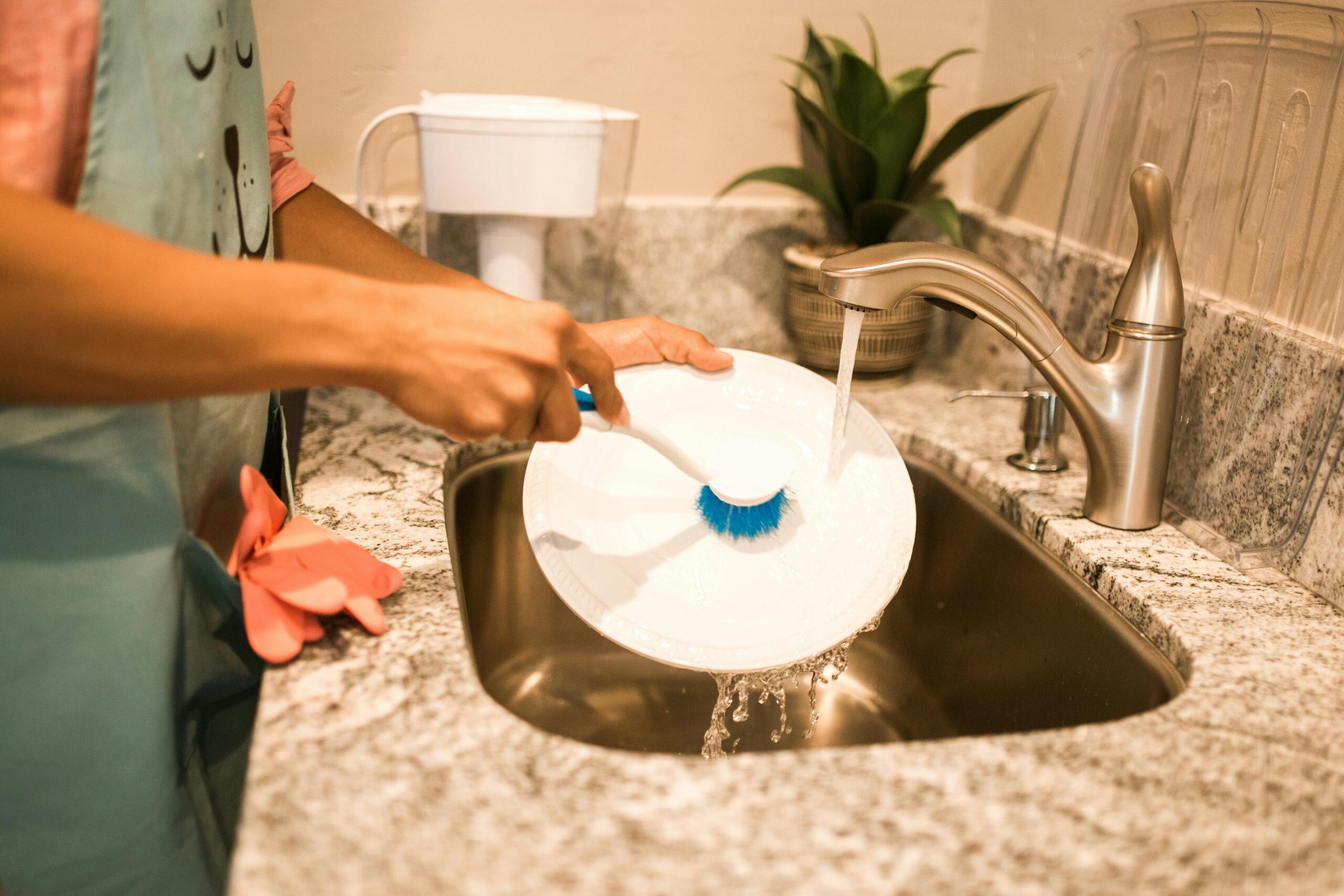 A person scrubbing a plate with running water in a modern kitchen sink.